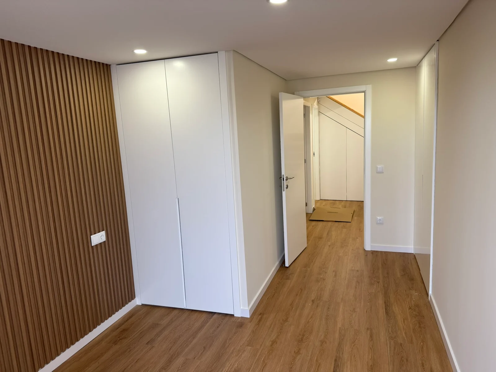 Interior com roupeiro branco, pavimento de madeira e parede ripada